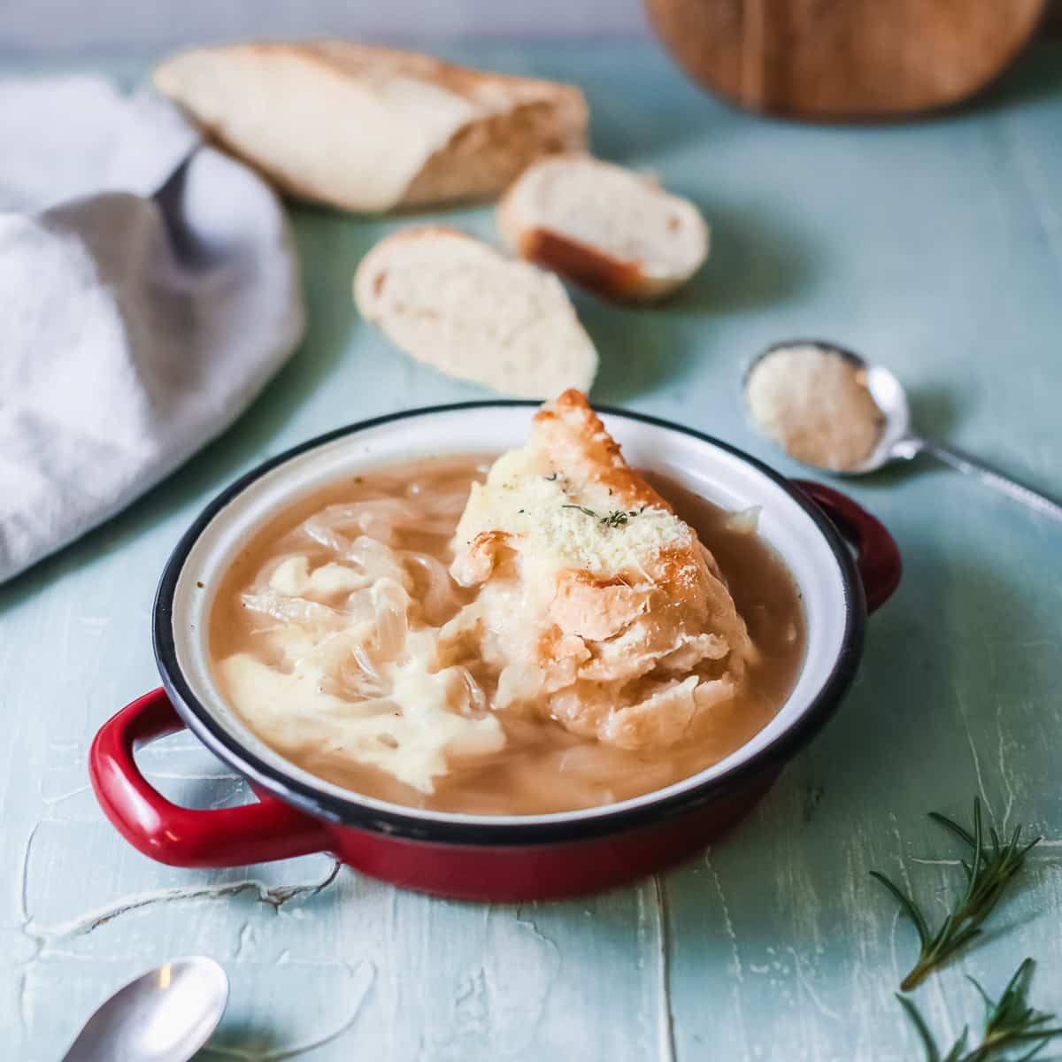 Copycat Panera French onion soup in a red enamel bowl topped with cheesy toasted bread