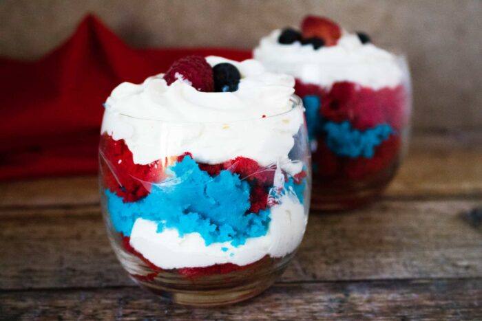 Two 4th of July Mini Cake Trifles served in glass dessert cups and garnished with araspberry and blueberry