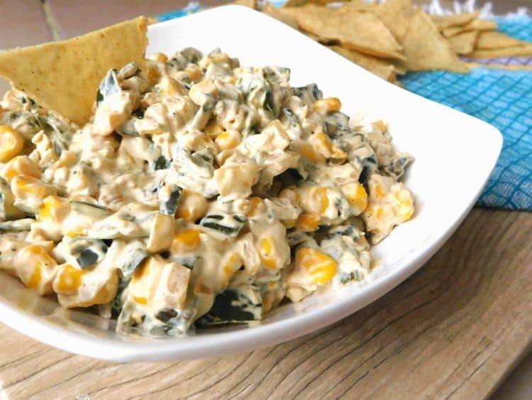 Creamy poblano pepper and corn dip in a white bowl on a wooden table with tortilla chips