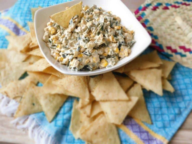Roasted poblano pepper dip in a white bowl set on a pile of tortilla chips