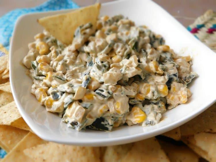 Close-up of creamy poblano and corn dip in a white bowl with a tortilla chip