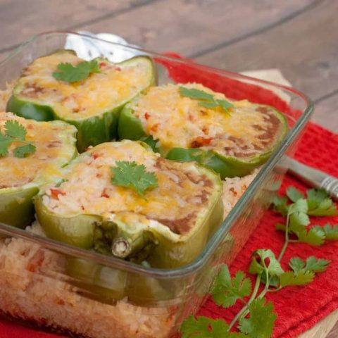 Mexican stuffed peppers topped with melted cheese and cilantro in a glass baking dish of Mexican rice