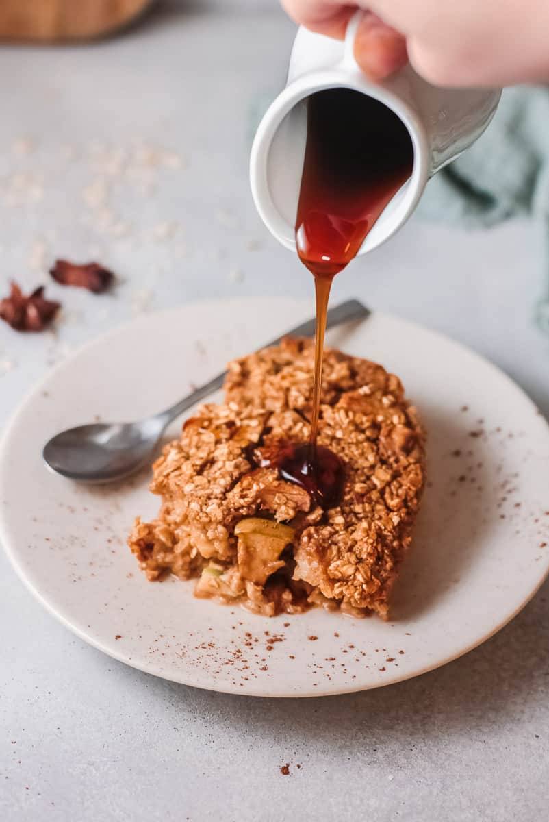Pouring syrup over a slice of apple cinnamon baked oatmeal on a plate