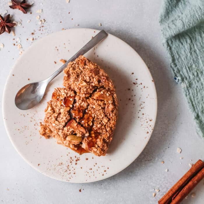 Slice of apple cinnamon baked oatmeal on a white plate with a spoon, cinnamon sticks, and star anise