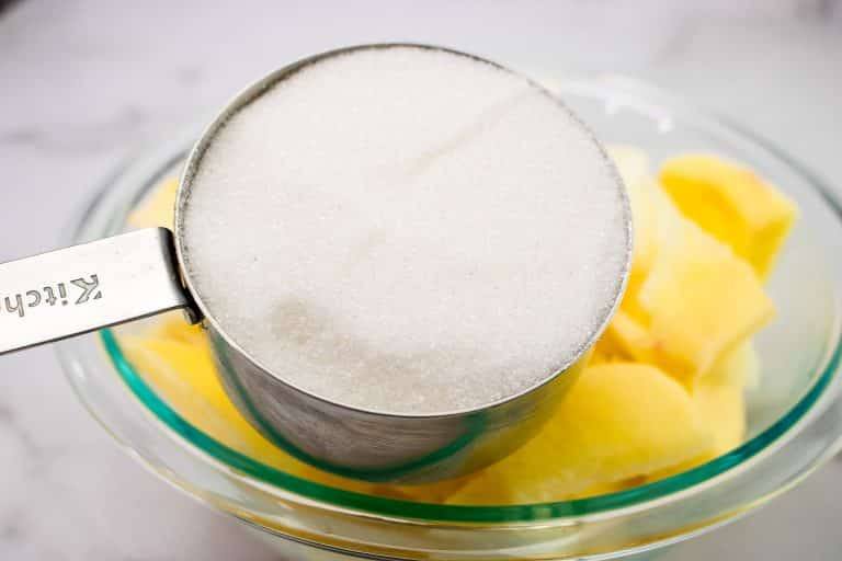 Granulated sugar measured over sliced apples in a glass bowl