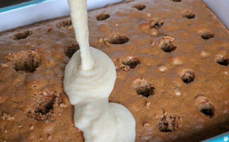 Baked cake with holes poked using a wooden spoon handle while apple pie filling is poured over the top