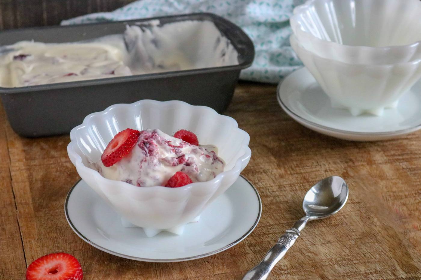 Berry Pie No-Churn Ice Cream in a white scalloped bowl on a white saucer next to a silver spoon and a strawberry slice on the table