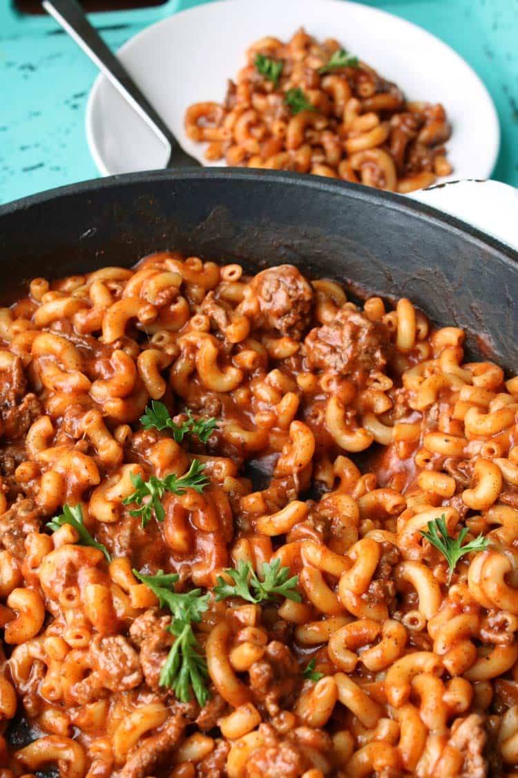 Skillet of chili mac with ground beef, elbow macaroni and tomato sauce, garnished with parsley