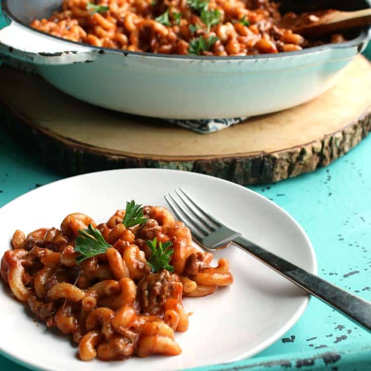 Serving of chili mac on a white plate with a fork, with the skillet of chili mac in the background