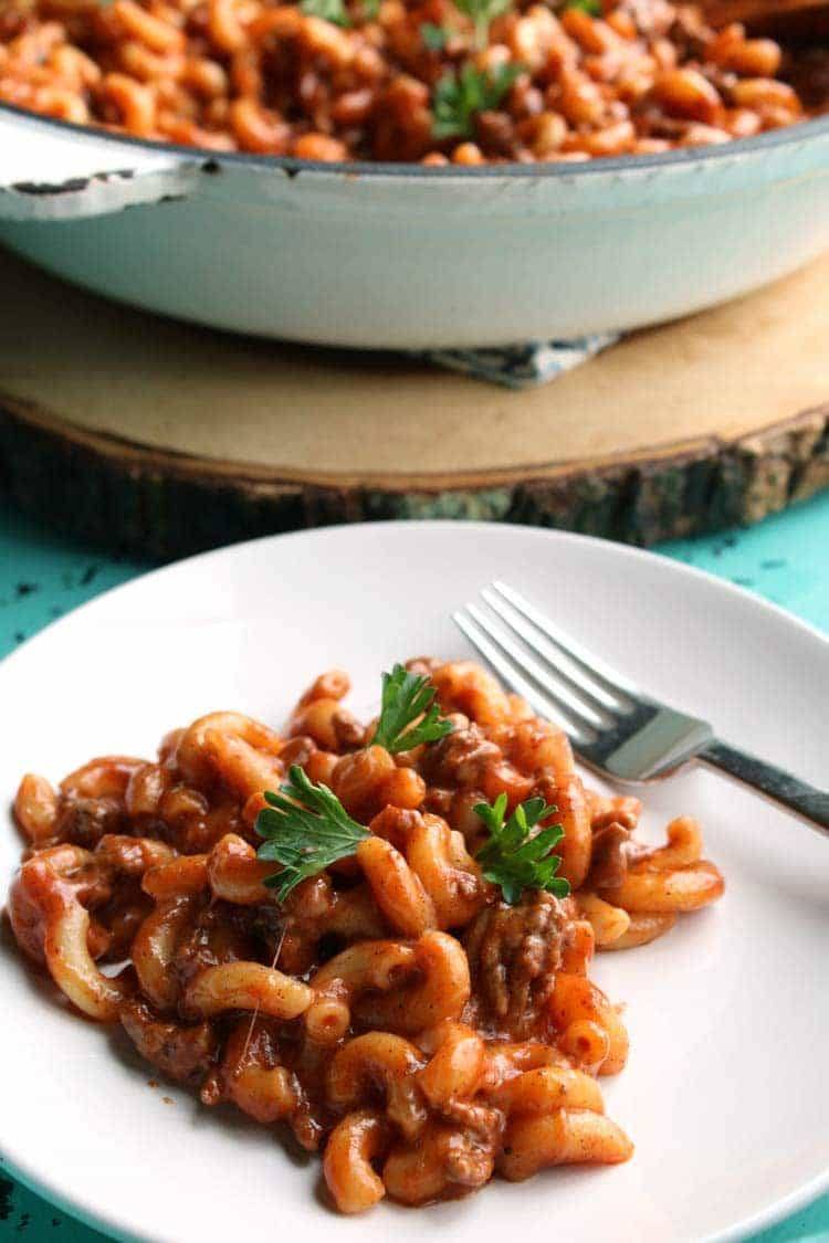 Plate of chili mac with ground beef and fresh parsley in front of a white skillet