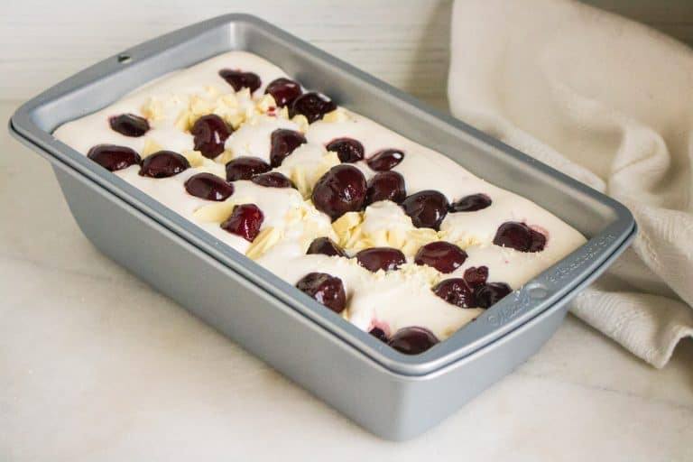 metal loaf pan filled with the no churn ice cream mixture and topped with black cherries and white chocolate chunks