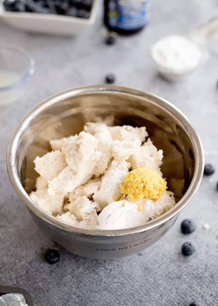 Broken up sugar cookie dough in bowl with lemon zest and flour.