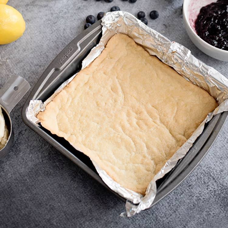 Half of sugar cookie dough pressed into the bottom of a 9x9 pan lined with foil.