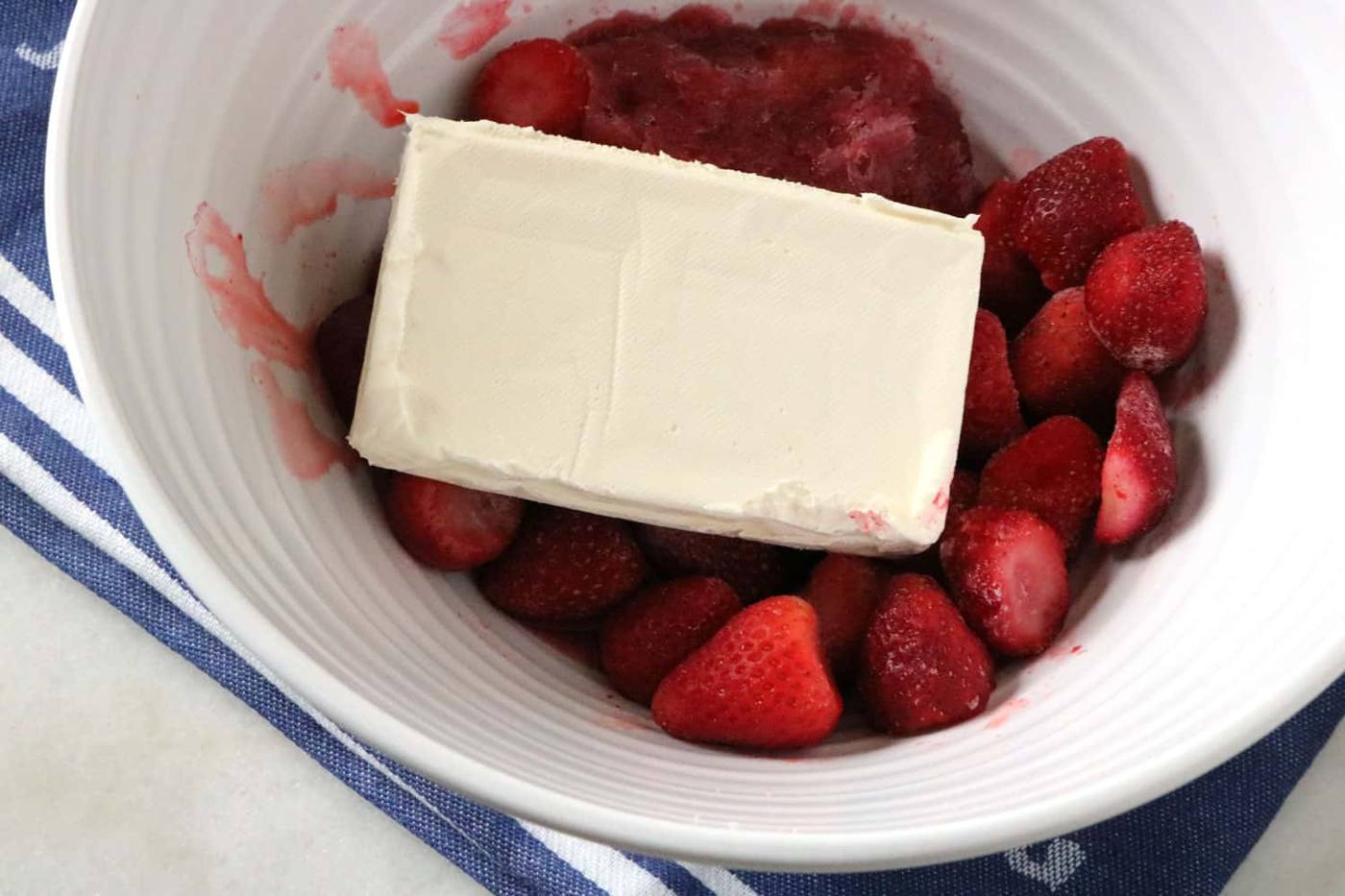 strawberries, cream cheese, and strawberry daiquiri mix in a white mixing bowl