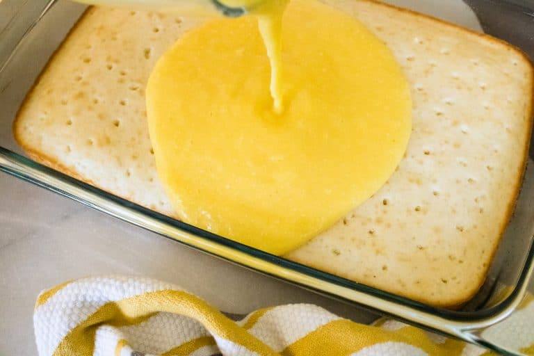 yellow boozy pineapple pina colada poke cake being poured onto white cake in pan