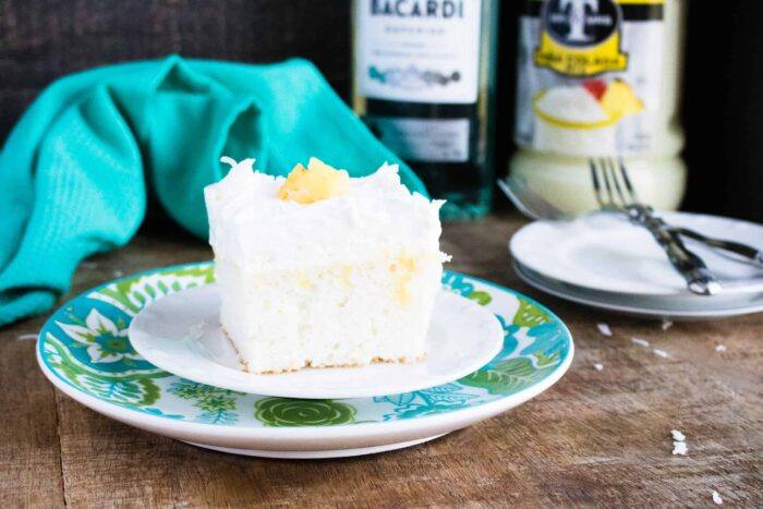 A slice of Boozy Pineapple Pina Colada Poke Cake served on a blue print dessert plate with a folk and blue cloth napkin