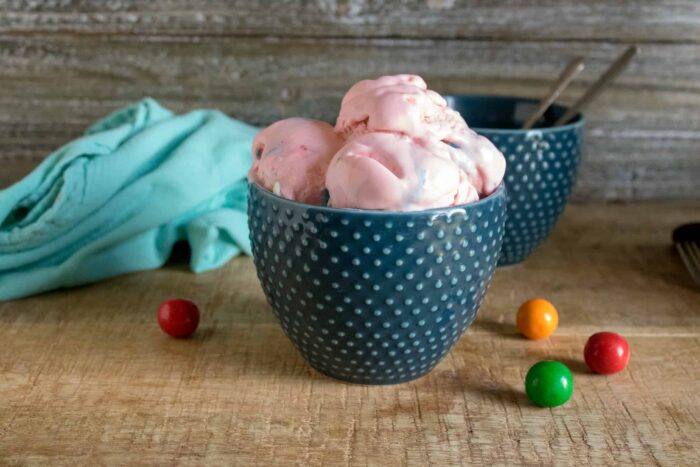 Bubble gum no-churn ice cream served in a blue polka-dot bowl next to a blue cloth napkin and multi-colored gum balls on a wood table