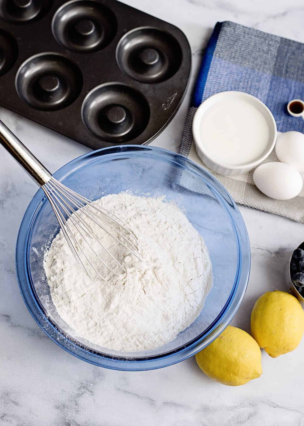 donut baking pan, blue glass bowl with flour and whisk, 2 lemons