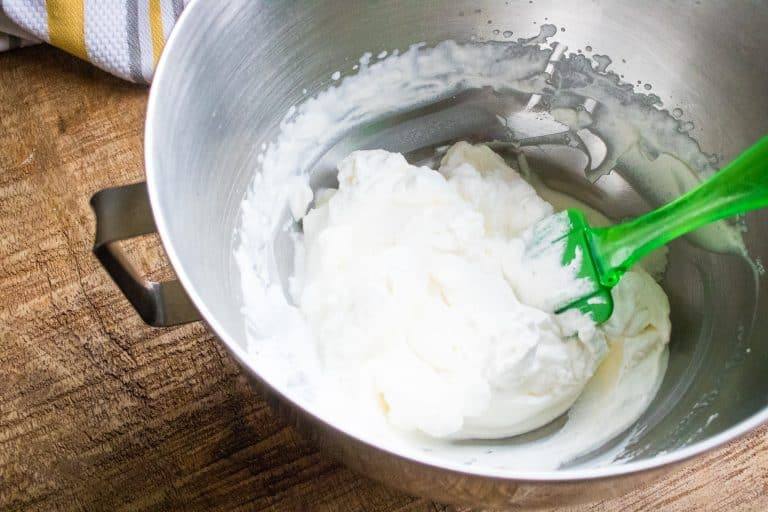 completed filling for cannoli cream cake roll minus chocolate chips in a silver bowl with green spatula