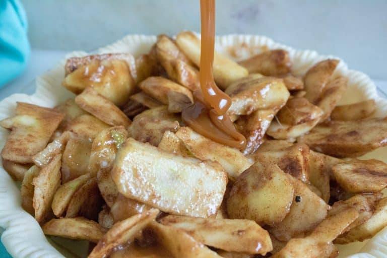 pie shell filled with apples for Caramel Apple Crumble Pie being drizzled by caramel sauce