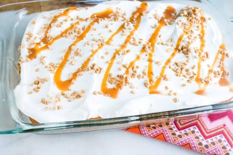 Finished Caramel Toffee Poke Cake in a 13x9 clear glass sheet pan set on top of a red and pink print cloth napkin