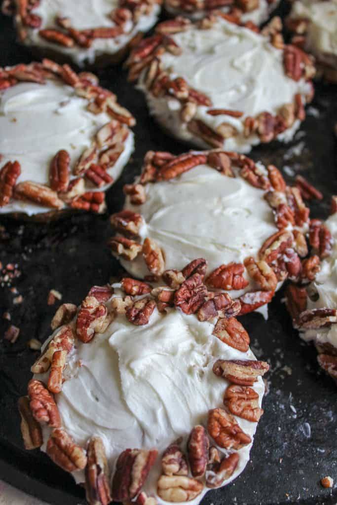carrot cake cookies baked and covered with cream cheese frosting and pecans around edges