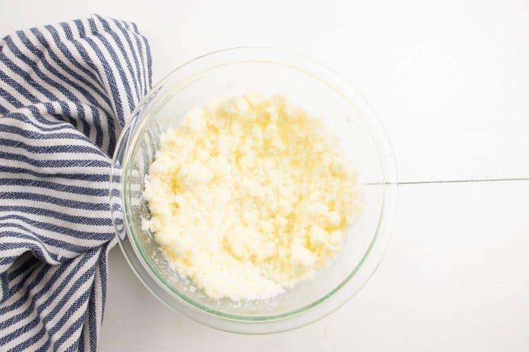wet ingredients for making cheesecake brownies in a glass bowl next to a blue striped kitchen towel