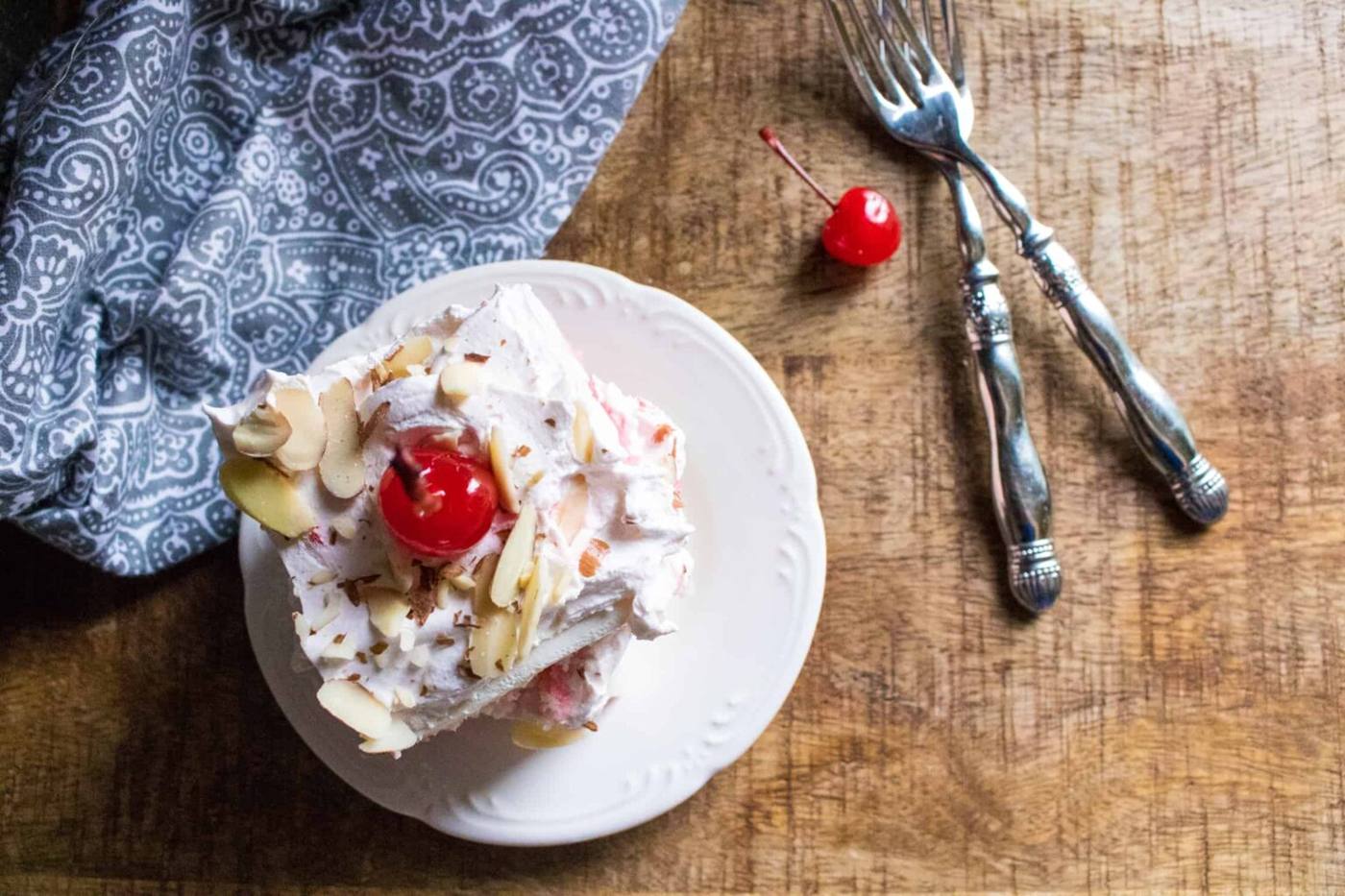 Cherry almond poke cake served on a white plate next to a blue print napkin and forks