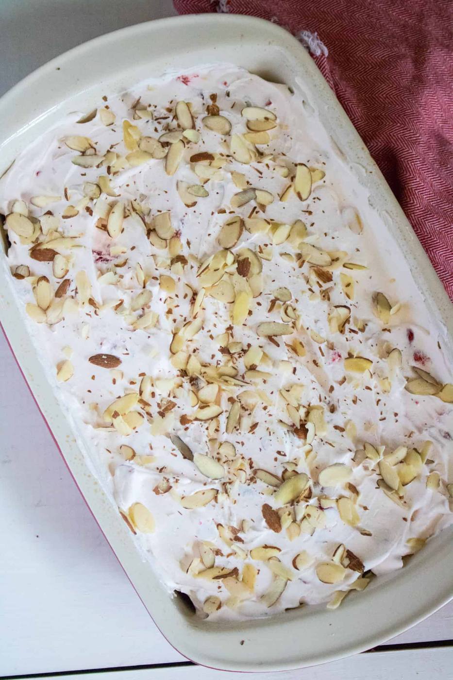 Finished cherry almond poke cake with whipped topping and sliced almonds