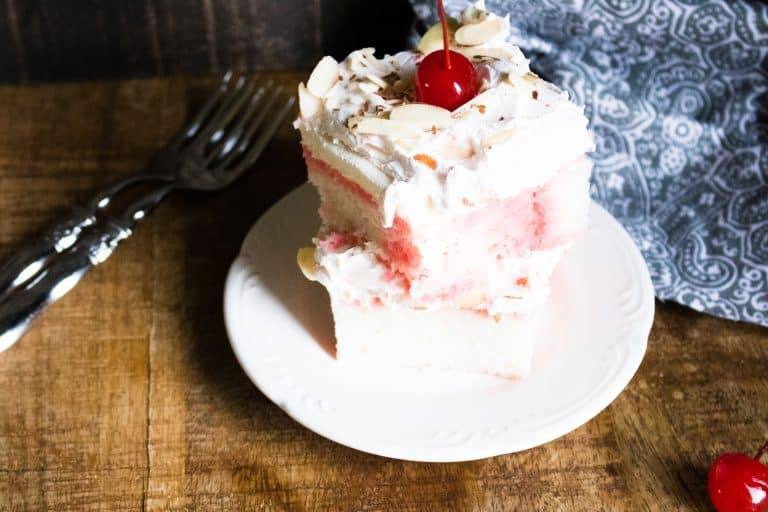 slice of cherry almond poke cake and served on a plate and topped with a maraschino cherry