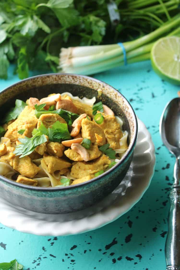 Chicken curry with noodles in a dark bowl with lime, green onions and fresh herbs