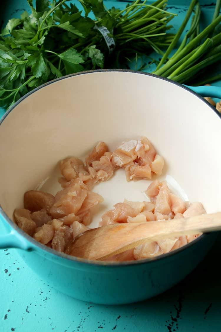 Cubed chicken cooking in olive oil in a teal Dutch oven