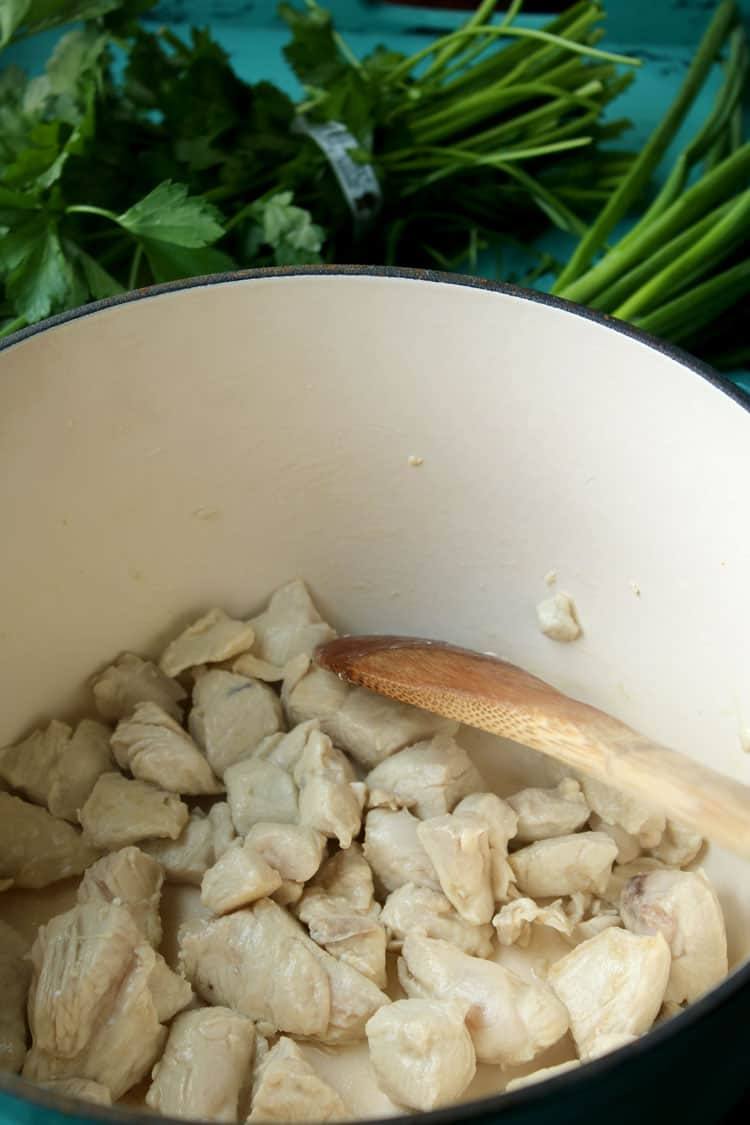 Browned cubed chicken in a Dutch oven with a wooden spoon