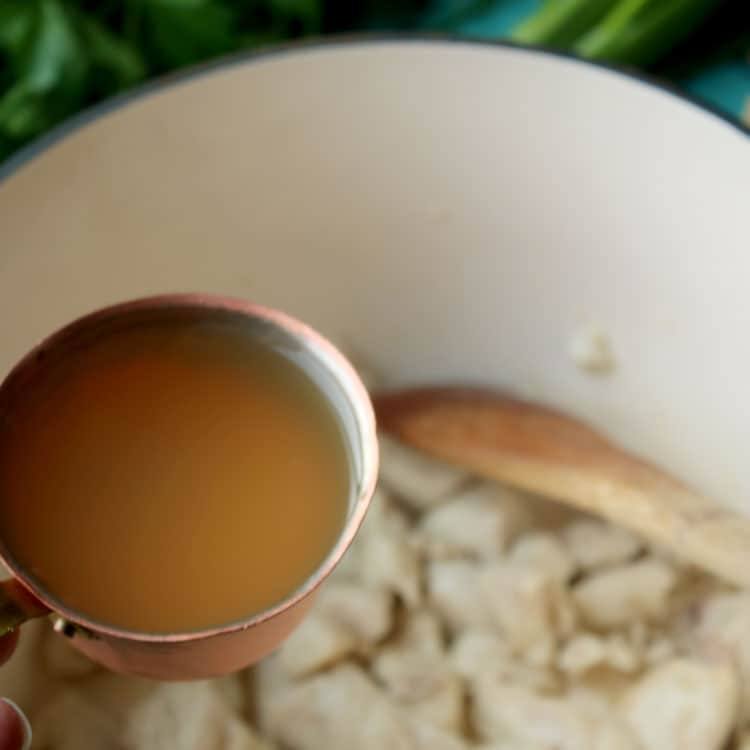 Pouring chicken broth over cooked chicken in a Dutch oven
