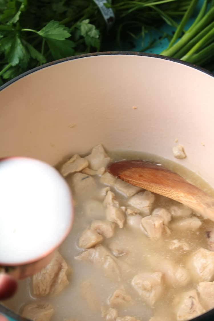 Adding coconut milk to chicken and broth in a Dutch oven