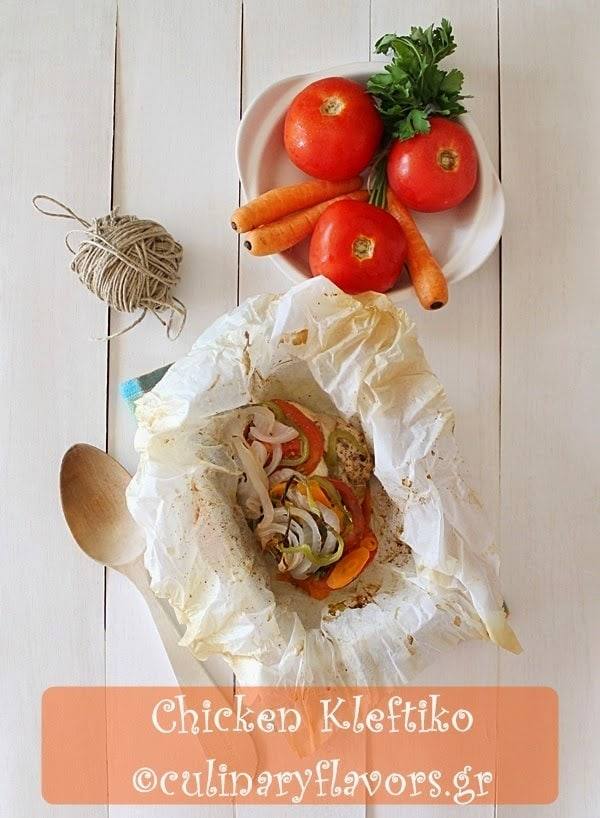 Chicken kleftiko baked in an open parchment packet with tomatoes, carrots, parsley and a ball of kitchen twine on a white table