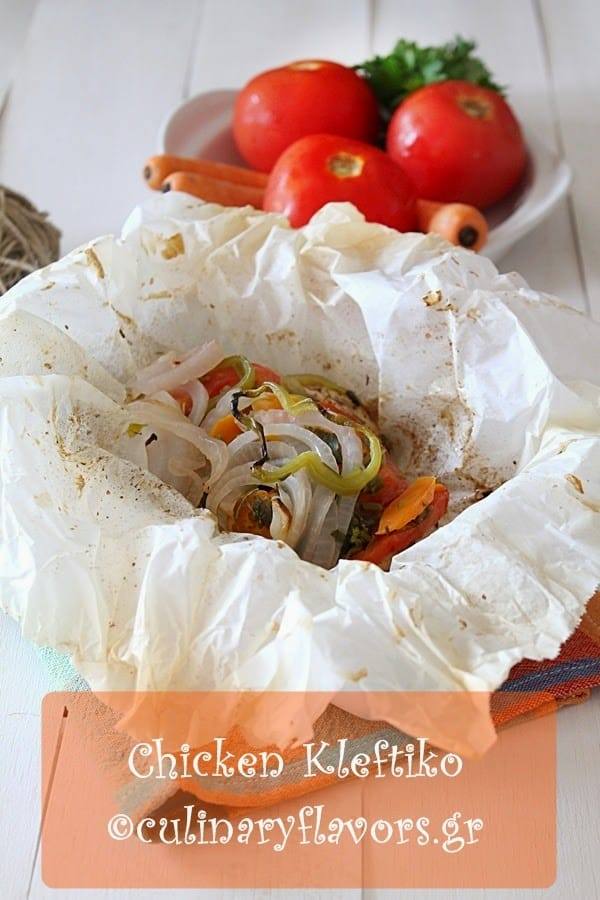 Greek chicken kleftiko in a parchment paper packet topped with onion, green pepper, tomato and carrot slices