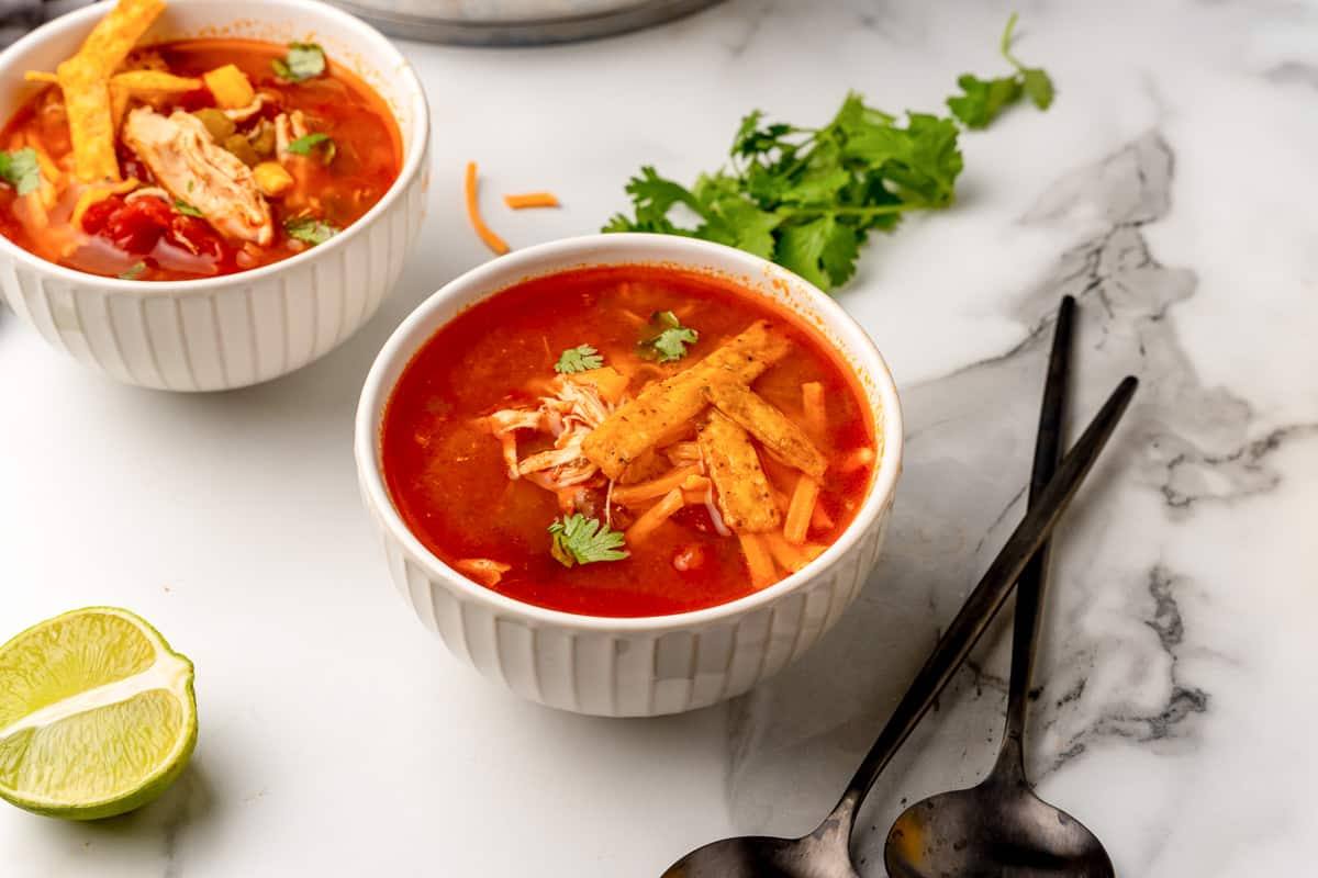 Two bowls of southwest chicken soup on a marble counter with lime wedges and cilantro