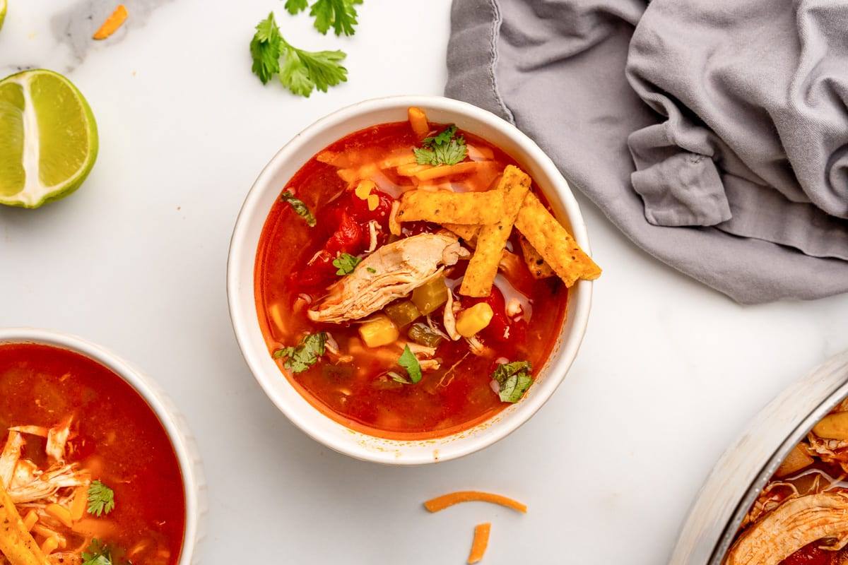 Bowl of Tex-Mex southwest chicken soup with tortilla strips, lime wedges and a gray napkin