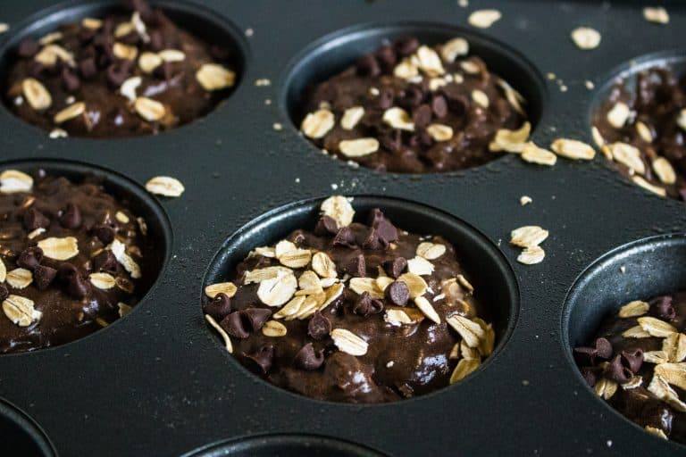 dark gray muffin tin will with batter for for Chocolate Chocolate Chip Oatmeal Muffins with oats sprinkled on top