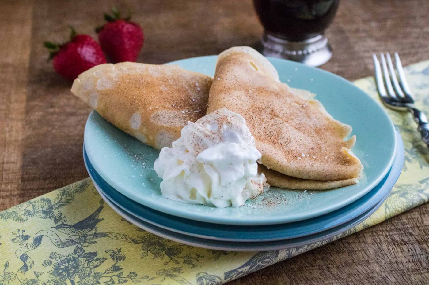 Snickerdoodle Crepes served on a blue plate next to a yellow print napkin and silver spoon