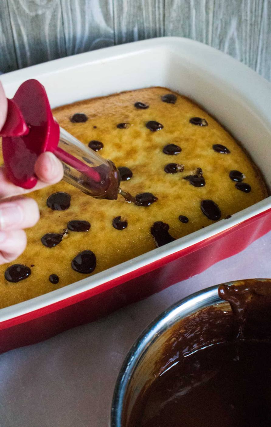 the poked holes in a white sheet cake being filled with chocolate ganache using a pastry cream injector
