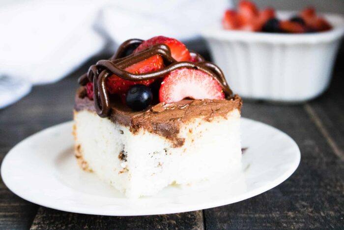 Chocolate Ganache Poke Cake with Berries sliced and served on a white dessert plate