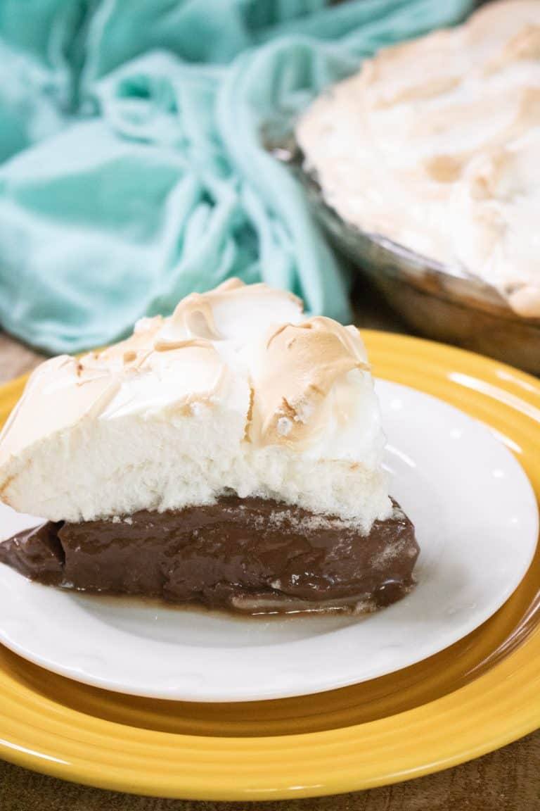 chocolate meringue pie set on white and yellow plates with a blue towel in the background and the pie to the top right
