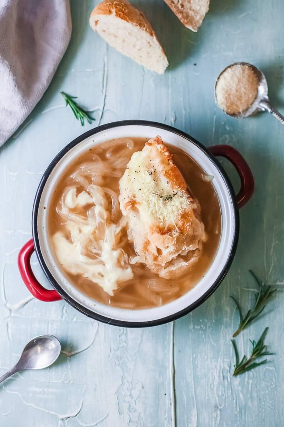 Bowl of French onion soup topped with cheesy bread next to sliced baguette