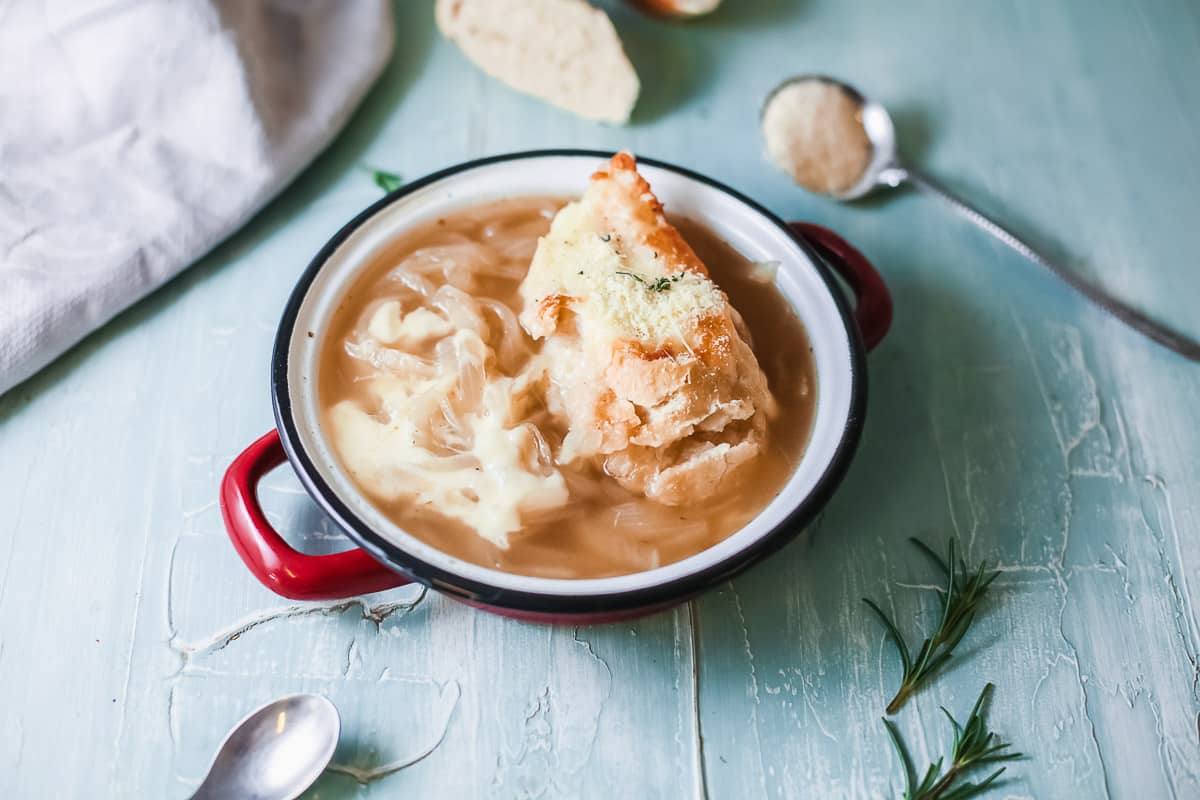 Side view of copycat Panera French onion soup in a red enamel bowl