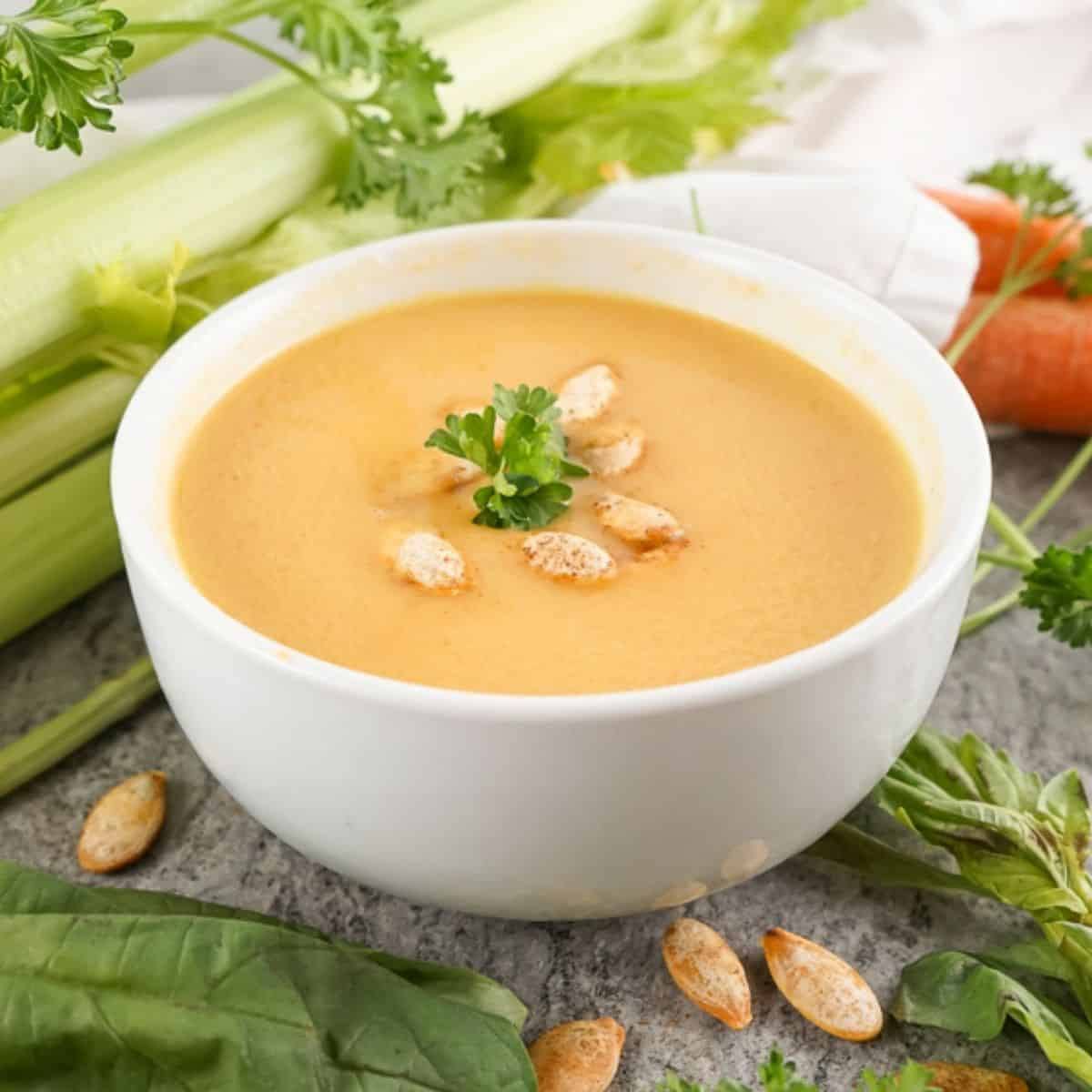 White bowl of copycat Panera autumn squash soup topped with toasted pumpkin seeds and parsley