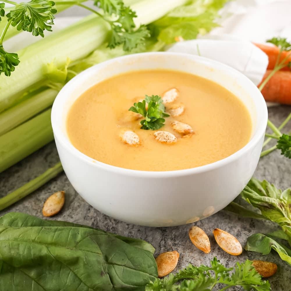 Close-up of a white bowl of copycat Panera autumn squash soup with pumpkin seeds and fresh parsley