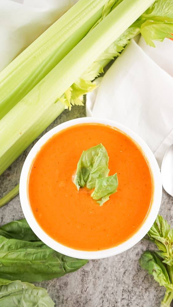 Bowl of copycat Panera tomato soup topped with fresh basil next to celery