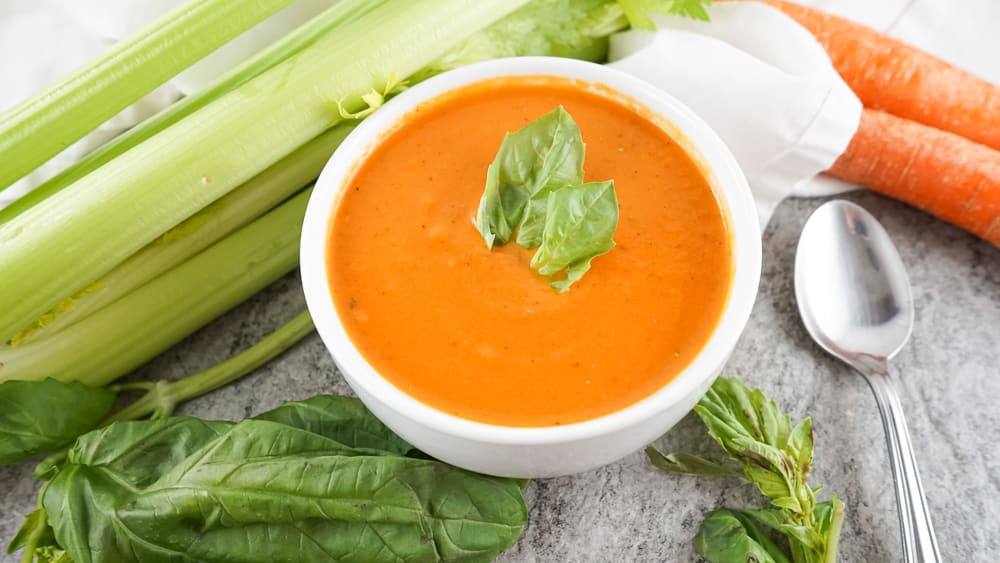Bowl of homemade Panera-style tomato soup with a spoon and fresh basil
